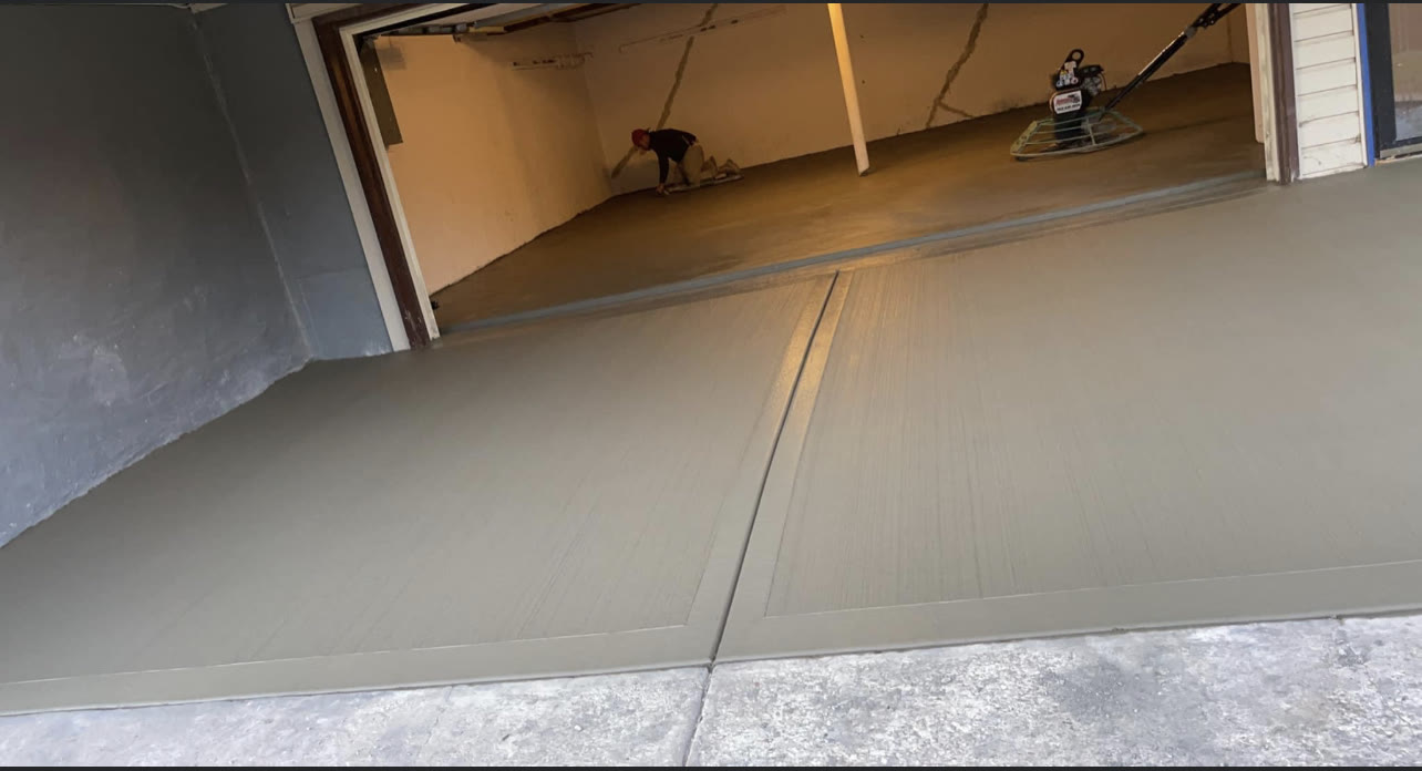 Freshly poured and power-troweled basement concrete floor, worker finishing the surface in the background