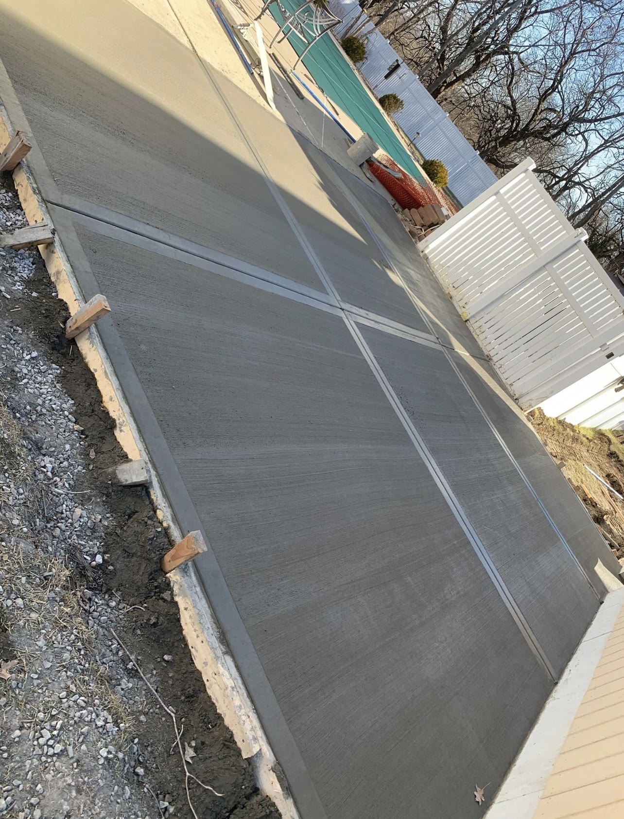 New concrete patio area next to a backyard pool, white vinyl fence and pool cover visible