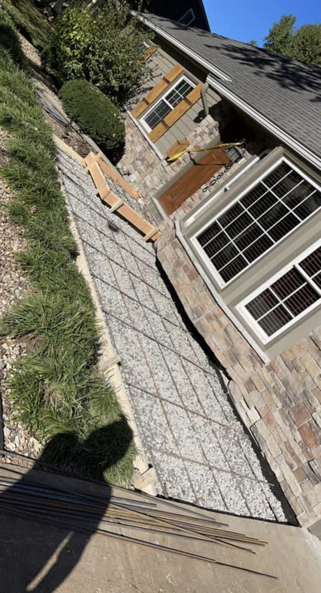 Rebar grid laid over a compacted gravel base, ready for a concrete pour alongside a home